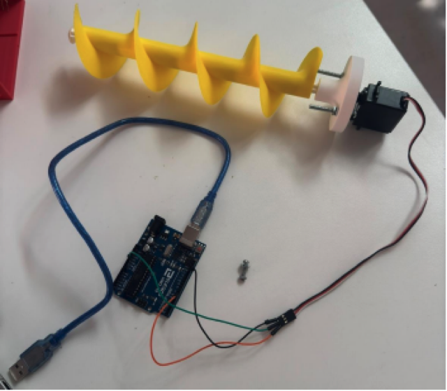 The yellow 3D-printed auger screw coupled to a servo motor and wired to an Arduino on a workbench.
