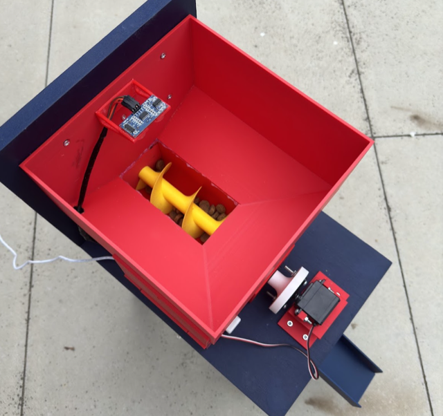 Top-down view of the finished feeder with the lid removed, showing the auger screw and electronics inside the red hopper.